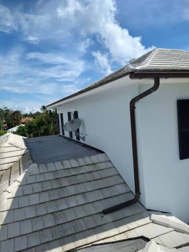 Dark seamless gutter and downspout installation on a white home with a tile roof