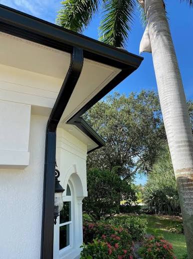 Dark seamless gutter and downspout detail at a residential roof edge