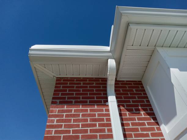 White seamless gutter and downspout assembly mounted to the roofline of a brick residential building