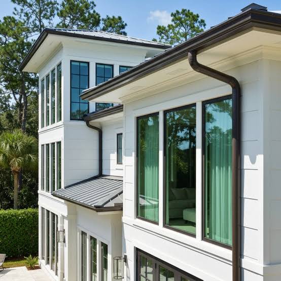 Modern residential exterior with dark seamless gutters and a downspout against a white facade and metal roof